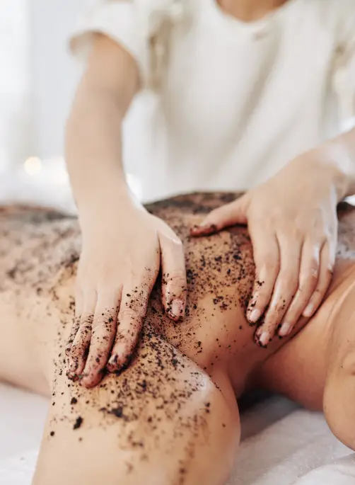 A woman massages essential oils and herbs into a man's back during a body prep session