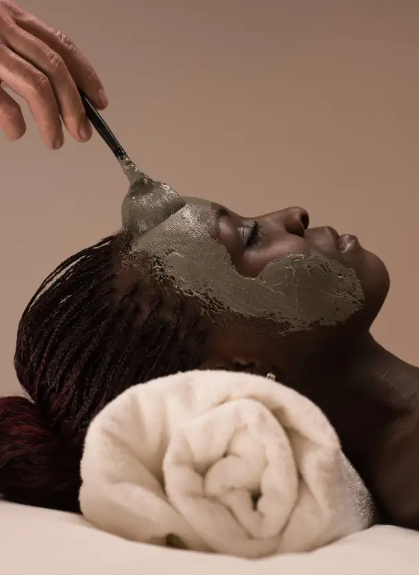 A young woman is resting her head on a spa towel while an expert facial technician at SurePose applies a soothing facial mask