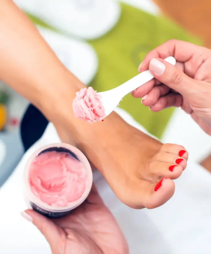 An aromatherapy mask is carefully applied to a woman's foot during a pedicure